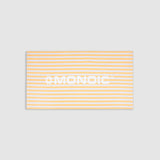 Monoic cotton towel with white background, bold yellow stripes, and “Monoic” written horizontally.