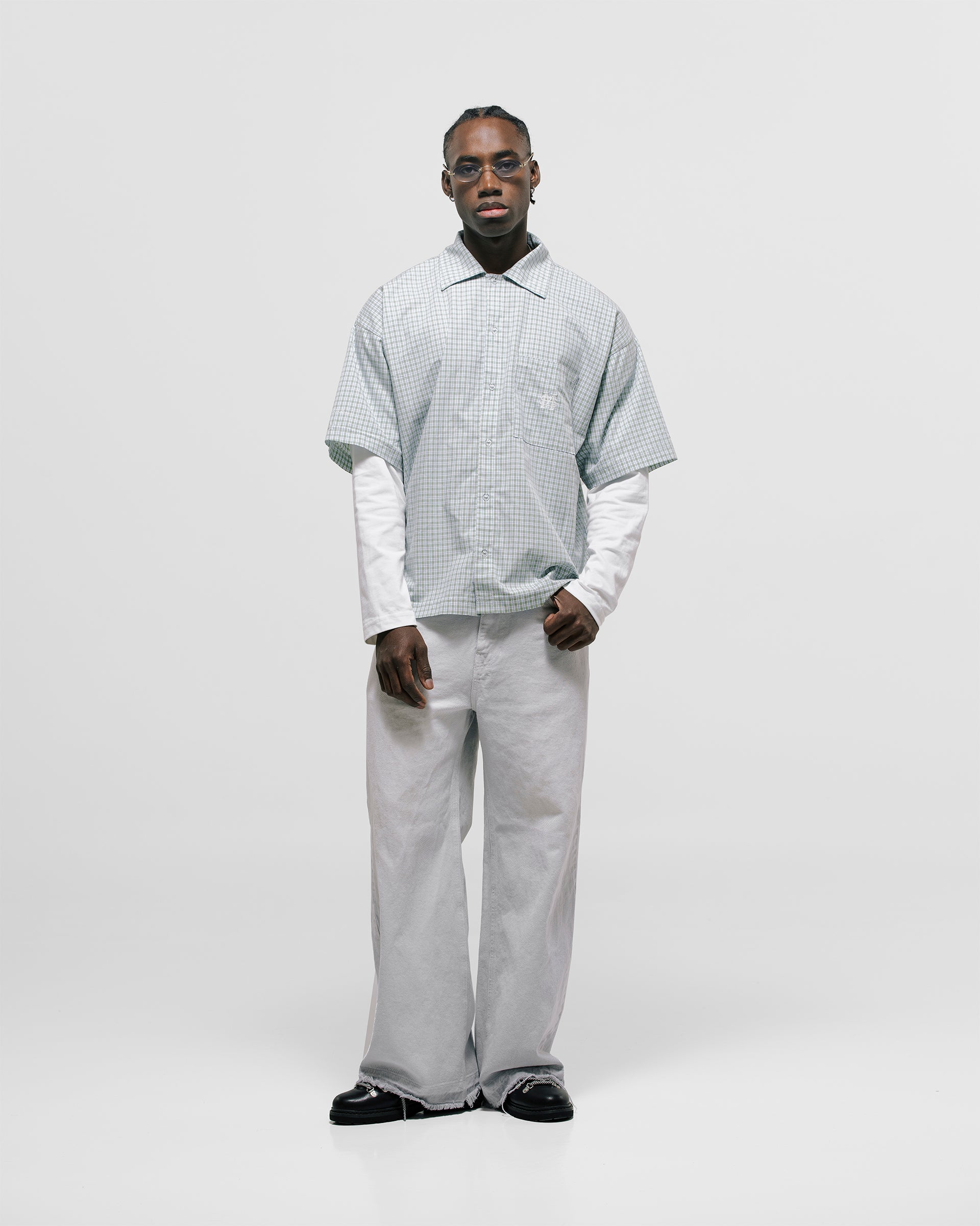 Checkered double sleeve shirt with light green, blue, and white plaid body, off-white contrast sleeves, boxy fit, and embroidered monogram on the chest pocket.