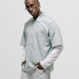 Checkered double sleeve shirt with light green, blue, and white plaid body, off-white contrast sleeves, boxy fit, and embroidered monogram on the chest pocket.
