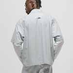 Checkered double sleeve shirt with light green, blue, and white plaid body, off-white contrast sleeves, boxy fit, and embroidered monogram on the chest pocket.